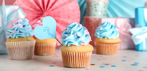 Delicious cupcakes with question mark, gift boxes and decorations on table against pink background. Gender reveal party concept