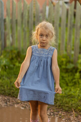 Puddle fun, outdoor education.  A preschool girl in a puddle is showing her wet dress, summer rural...