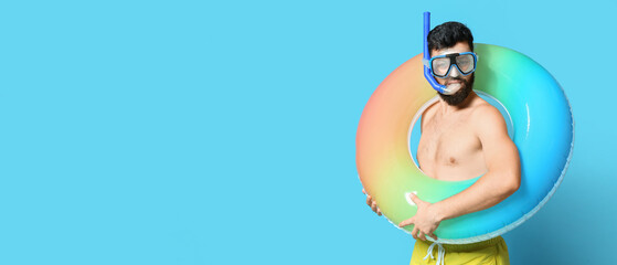 Young man with inflatable ring and snorkeling mask on color background