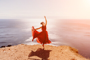 Woman red dress sea. Female dancer in a long red dress posing on a beach with rocks on sunny day....