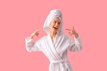 Young woman in bathrobe after shower pointing at hair towel on pink background