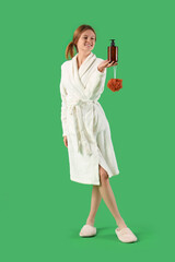 Beautiful young woman in bathrobe, with bast wisp and shower gel on green background