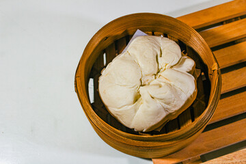 White, green bean-flavored buns are served on a dim sum basket with a wooden coaster