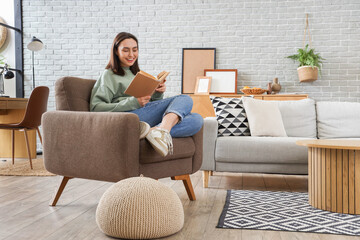 Happy young woman reading book in armchair at home