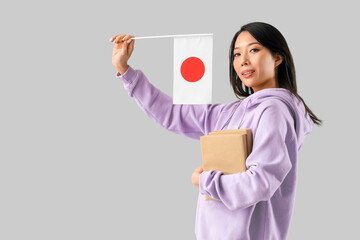 Female Asian student with books and flag of Japan on light background