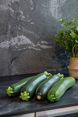 Aesthetic arrangement of fresh zucchini on a slate countertop, enhanced by their dark to light green gradient, complemented by a potted plant in a rustic kitchen.