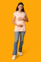 Happy young pregnant African-American woman on yellow background