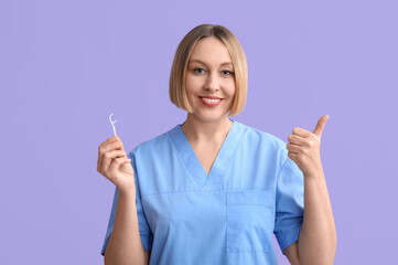 Female dentist with dental floss pick showing thumb-up on lilac background
