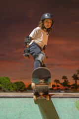 Child skateboarder standing on his skateboard on the edge of the ramp