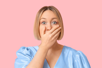 Shocked adult woman covering mouth on pink background