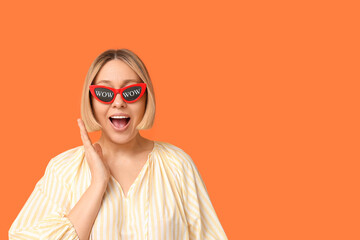 Surprised adult woman in eyeglasses with words WOW on orange background