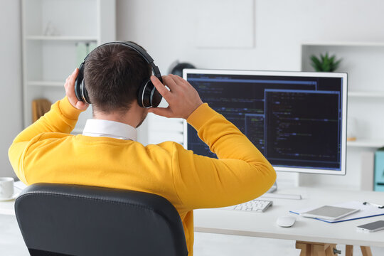 Male programmer in headphones working with computer in office, back view