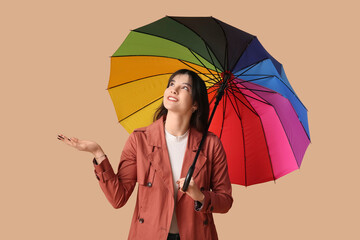 Young woman with opened colorful umbrella on beige background