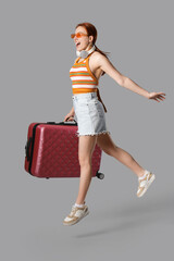 Female tourist with suitcase jumping on grey background