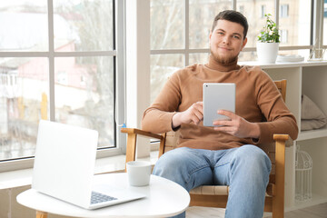 Young bearded man using tablet computer in armchair near window at home