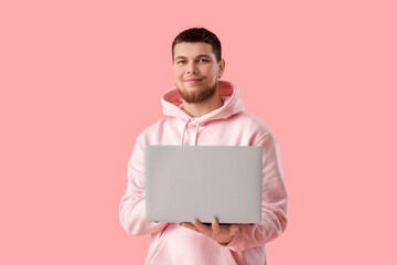 Young bearded man using laptop on pink background