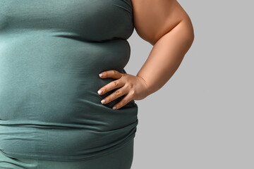 Young overweight woman on grey background, closeup. Weight loss concept