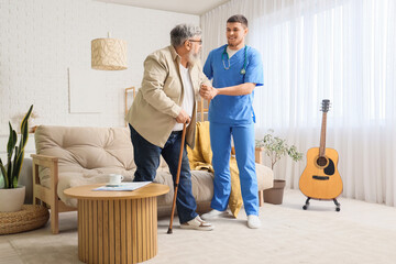 Young caregiver taking care of senior man with stick at home