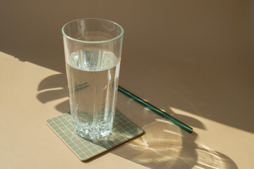 Glass of water in neutral beige background with shadows of leaves. Natural glass recyclable...