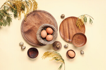 Table setting with Easter eggs, nest, trays and plants on light yellow background - obrazy, fototapety, plakaty