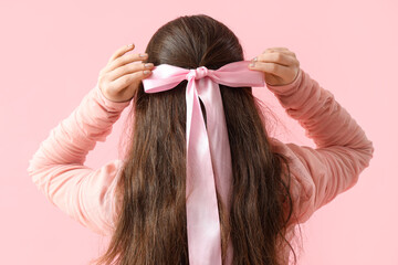 Stylish young woman with bow on her hair against pink background, back view