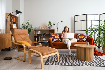Young woman using laptop on red sofa at home