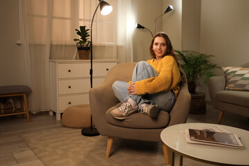 Young woman sitting on soft armchair at home in evening