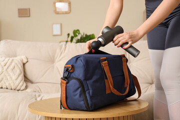 Sporty young woman putting percussive massager in bag at home, closeup