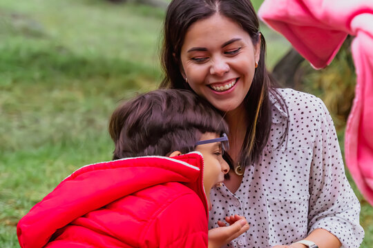 International Children Day. Latin mother having fun with her young children outdoors. Sitting on the ground playing with their hands. Concept of family. Single mother with two young children.