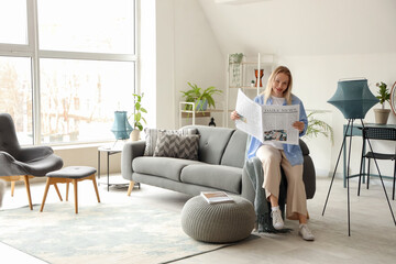 Young woman resting on sofa and reading newspaper in white living room