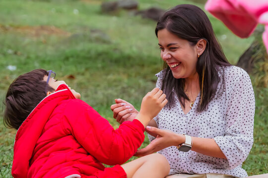 International Children Day. Latin mother having fun with her young children outdoors. Sitting on the ground playing with their hands. Concept of family. Single mother with two young children.
