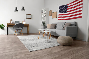 Interior of stylish office with modern workplace, laptop, cozy sofa and USA flag on white wall