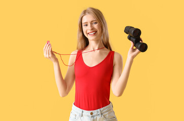 Young female lifeguard with binocular and whistle on yellow background