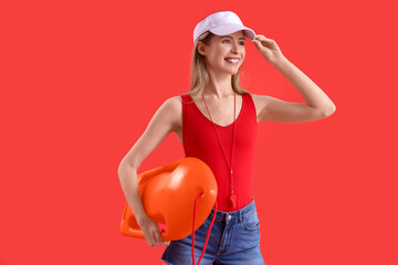 Young female lifeguard in cap with buoy on red background
