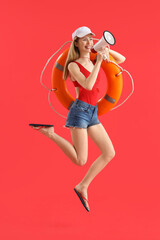 Young female lifeguard in cap jumping with rescue ring and megaphone on red background