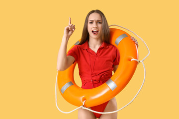 Young female lifeguard with rescue ring pointing at something on yellow background