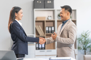 Young Asian businesswoman and middle-aged businessman, exemplifying pivotal moments, clear articulation, proliferation of ideas, and overcoming divisive challenges with successful handshakes.