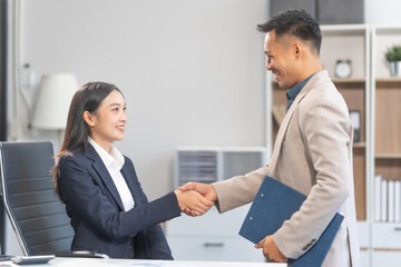 Young Asian businesswoman and middle-aged businessman, exemplifying pivotal moments, clear articulation, proliferation of ideas, and overcoming divisive challenges with successful handshakes.