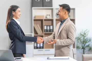 Fototapeta premium Young Asian businesswoman and middle-aged businessman, exemplifying pivotal moments, clear articulation, proliferation of ideas, and overcoming divisive challenges with successful handshakes.