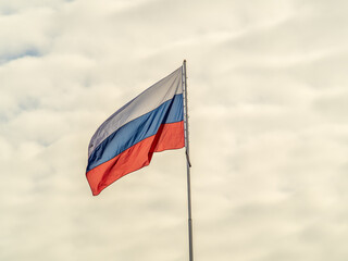 Russian tricolor flag waving in the wind against a blue sky.