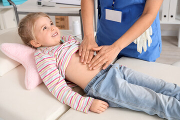 Female pediatrician examining little girl's belly on couch in clinic, closeup