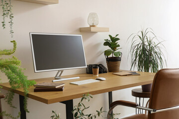 Modern workplace with computer monitor and houseplants near light wall in office