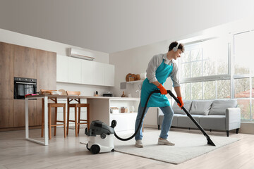 Male janitor with headphones cleaning carpet in kitchen