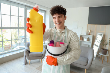 Young man with bucket of cleaning supplies at home