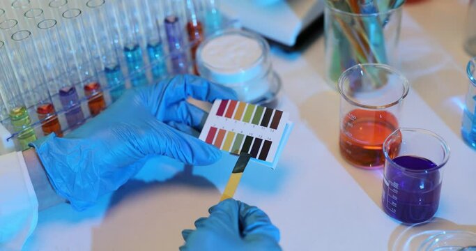 Scientist x holds a strip of litmus paper dipped in a purple liquid and observes color change, indicating acidity