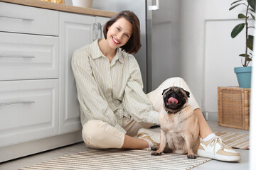 Young woman with cute pug dog sitting on floor in kitchen