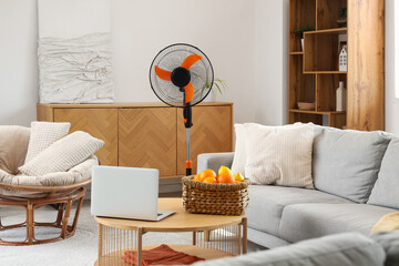 Interior of light living room with modern electric fan and laptop on coffee table