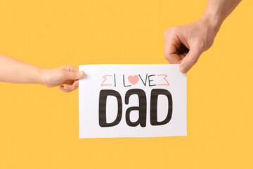 Father and daughter holding card with text I LOVE DAD on yellow background