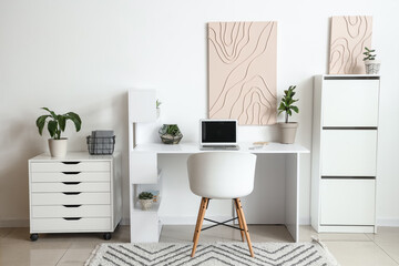 Interior of light office with modern workplace, laptop and pictures