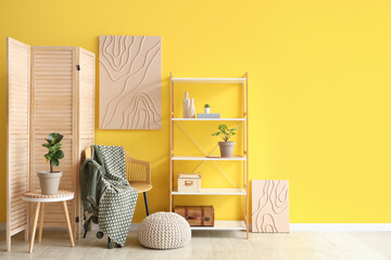 Interior of beautiful living room with armchair, shelving unit, coffee table and picture on yellow...